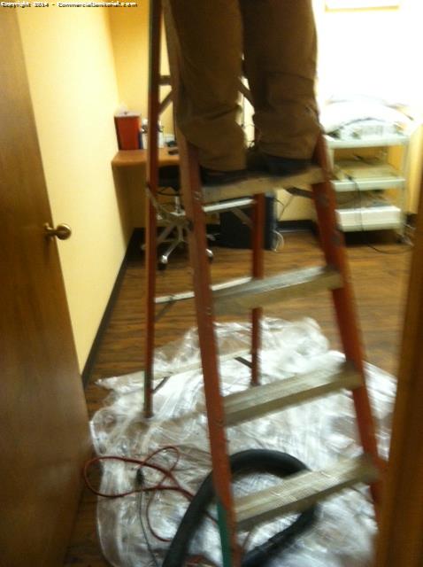 Cleaners are using a ladder to high dust an office